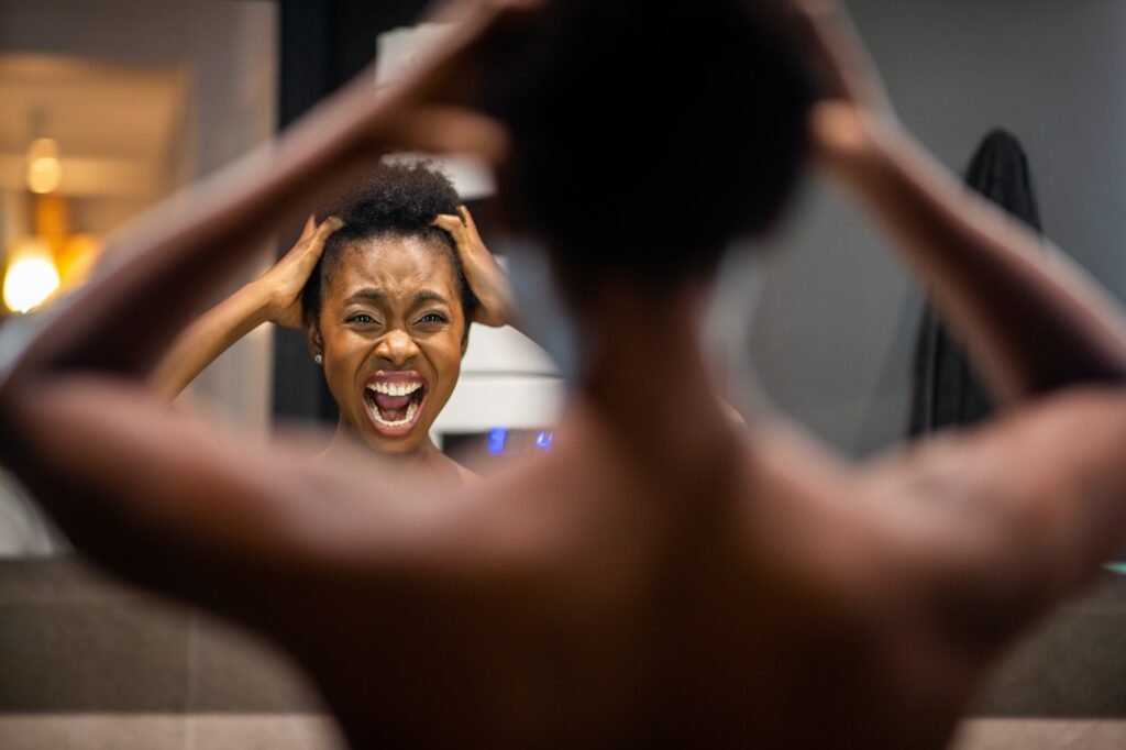 back of young african american woman adjusting hair in mirror and shouting